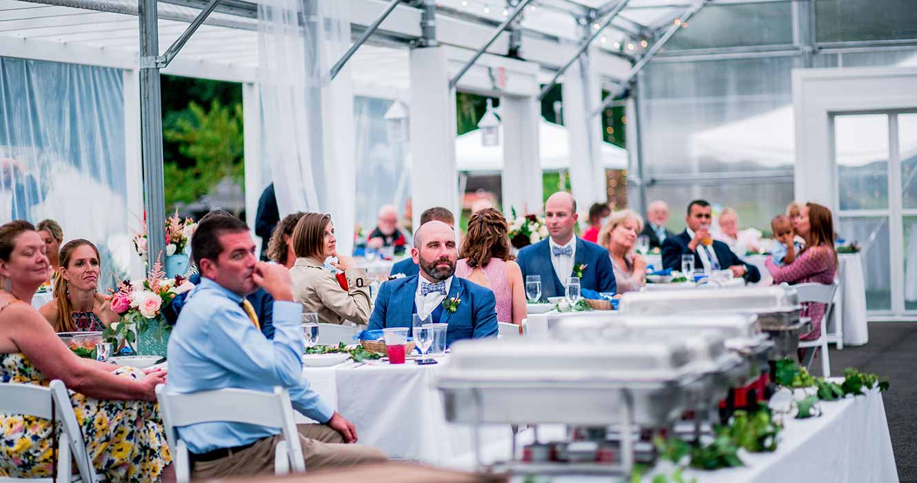 People sitting at tables in clear wedding tent